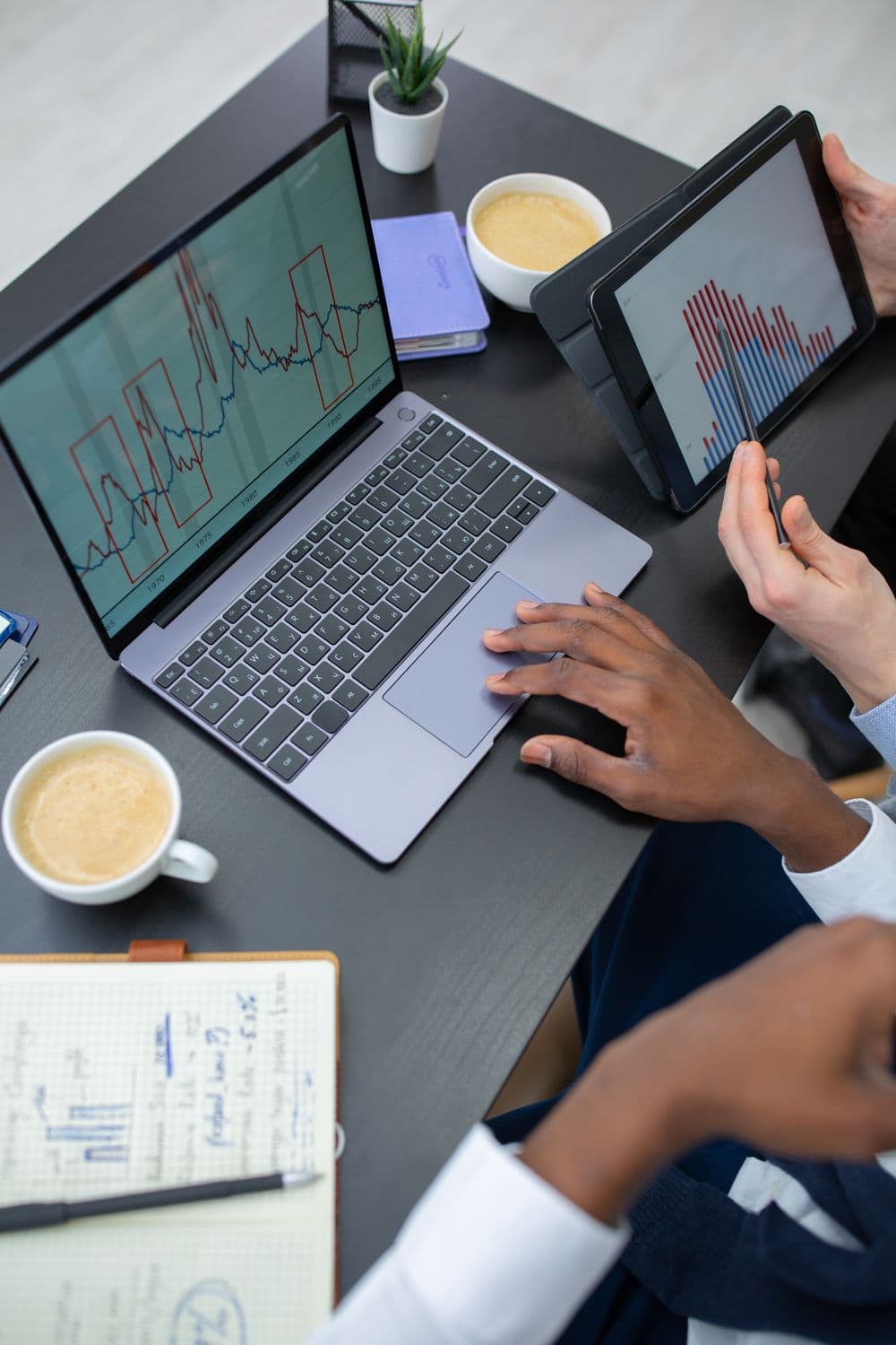 Colleagues comparing charts on a laptop and tablet at a shared desk